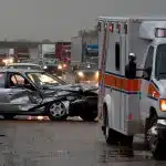 Totaled car on highway with ambulance nearby.