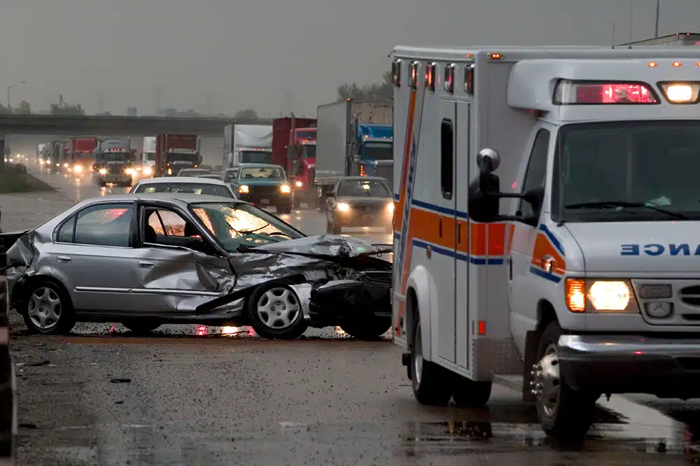 Totaled car on highway with ambulance nearby.